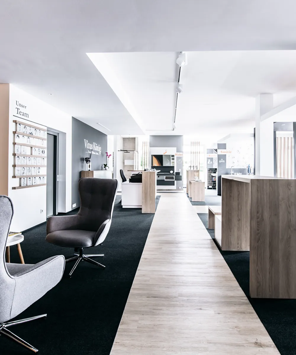Ein geräumiger und moderner Showroom mit grauen Loungesesseln und Holzelementen in einem hellen, minimalistischen Design. 
