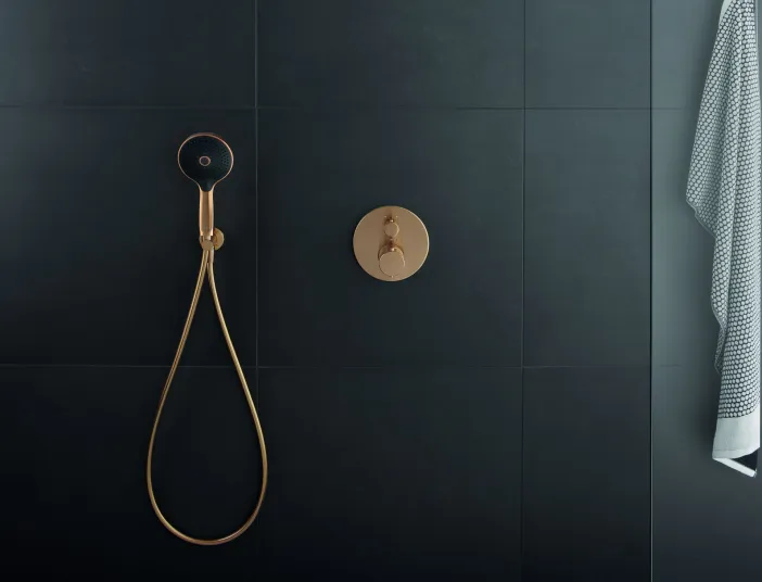 Ein luxuriöses Duschsystem mit einer goldenen Unterputzarmatur und einem schwarz-goldenen Duschkopf vor einer mattschwarzen gefliesten Wand.