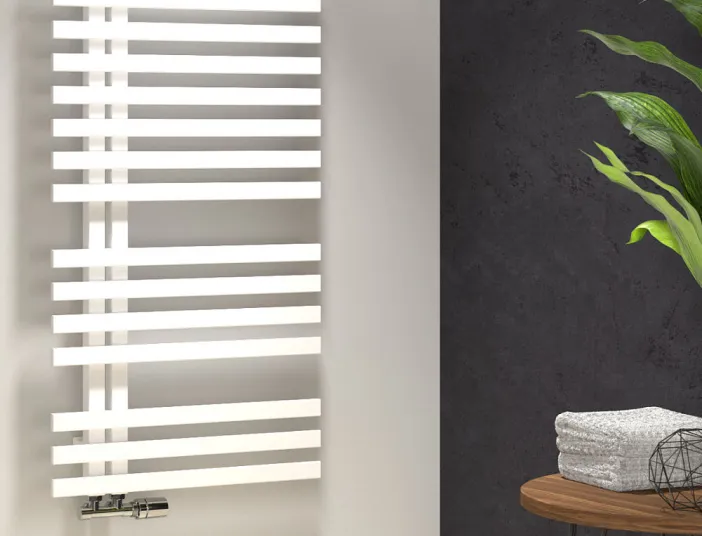 Ein weißer, moderner HSK Yenga Handtuchheizkörper mit horizontalen Streben ist an der Wand eines schick gestalteten Badezimmers angebracht. 