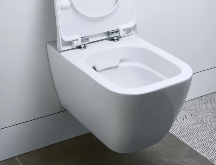 Ein modernes, wandmontiertes WC mit offener, hochgeklappter Toilettenbrille in einem minimalistischen Badezimmer. 