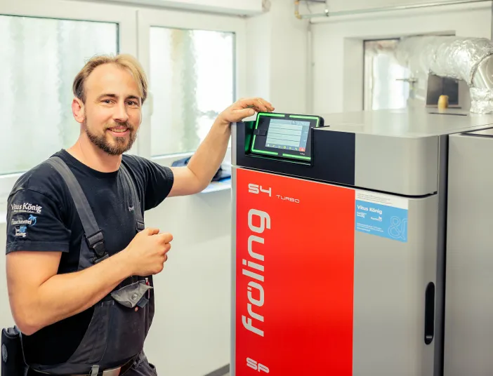 Ein Anlagenmechaniker von VitusKönig steht vor einer Pelletheizung mit modernem Display.