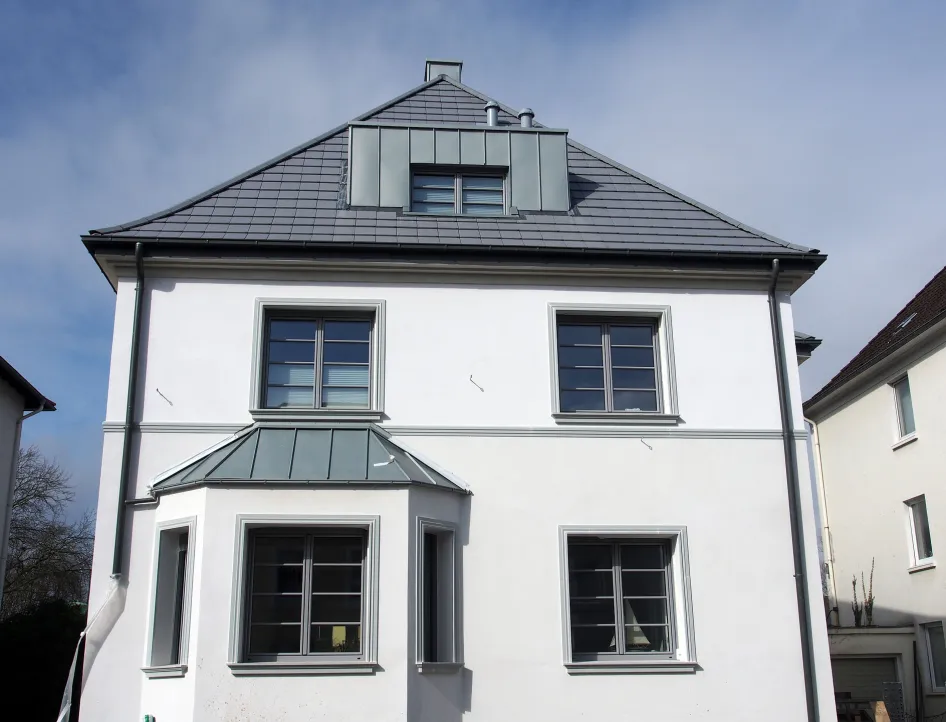 Ein modernisierter Altbau mit klaren Linien, neuer Fensterverglasung und einem grauen Satteldach. Die frisch renovierte Fassade wirkt gepflegt und stilvoll.